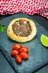 Delicious Lebanese food, legitimate sfihas on a black granite background with tomatoes, lemons with Keffiyeh in the background.