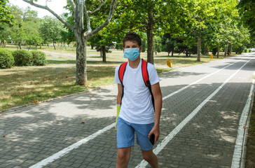 Close up cute young boy with protective mask on his face. Teenager in white t shirt wearing medical...