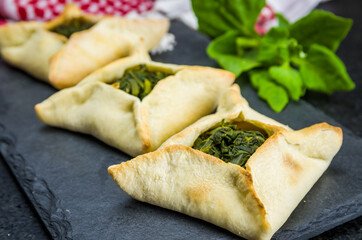 Delicious Lebanese food, spinach sfiha on black slate stone background and traditional Lebanese turban Keffiyeh.