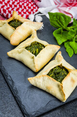 Delicious Lebanese food, spinach sfiha on black slate stone background and traditional Lebanese turban Keffiyeh.