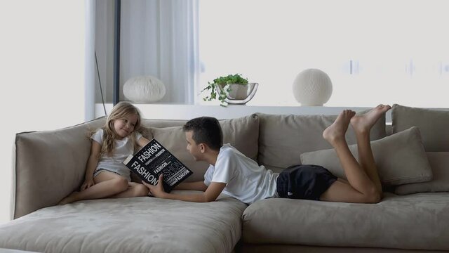 brother reading a book to his sister lying on the sofa
