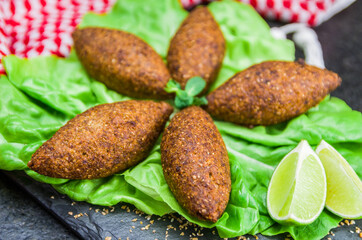Delicious Lebanese  food, kibbeh (kibe) with sauces and lemon on black slate stone and granite background with traditional keffyeh.