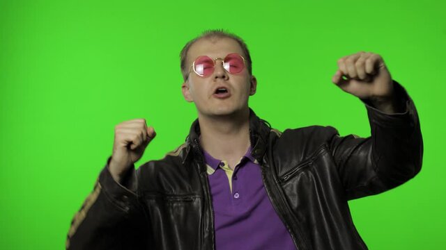 Playful rocker man in pink sunglasses moving in dance, smiling, making dab poses, gesture of success