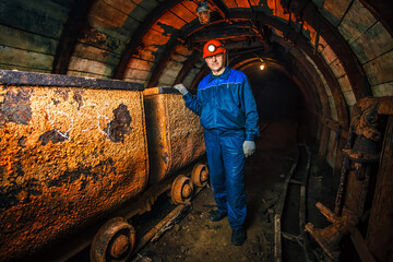 A miner in a coal mine stands near a trolley. Copy space.