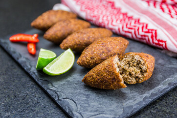 Delicious Lebanese  food, kibbeh (kibe) with sauces and lemon on black slate stone and granite background with traditional keffyeh.