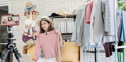 The attractive young woman is selling products, clothing, cosmetics through smartphones. From the room in the house Bright smiley face. Live Sale Concept.