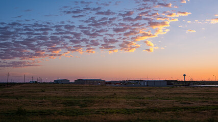 Colorful dark dawn sunrise in Snyder Texas with industrial building, warehouses or storehouses and factory by farm field with electricity pylons