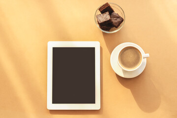 Fototapeta na wymiar Notebook, coffee cup and chocolate cake. Cosy workplace, work at home concept. Light orange background, top view, flat lay
