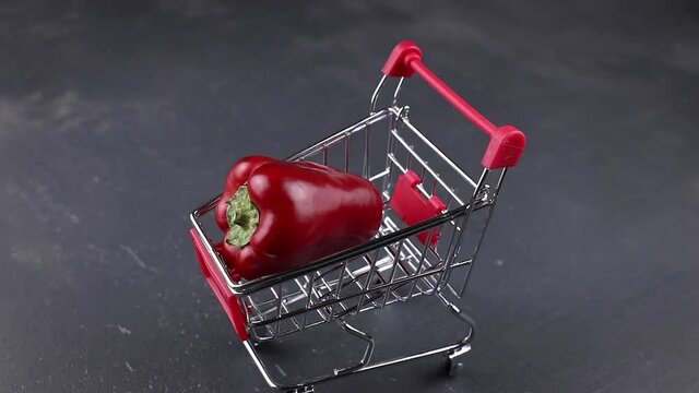 beautiful red bell pepper with shopping cart rotating on a dark stone background. concept of sales with copy space
