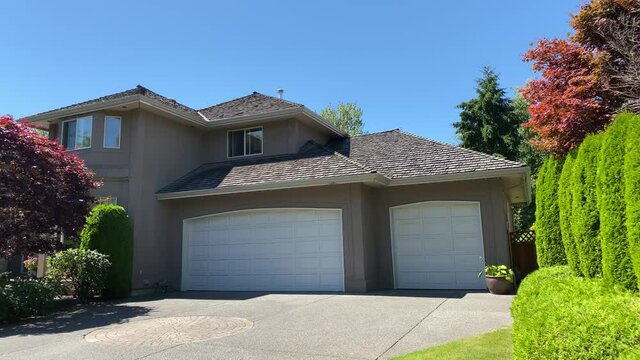 Establishing shot of two story stucco luxury house with garage door, big tree and nice landscape in Vancouver, Canada, North America. Day time on September 2020. Tilt up.
