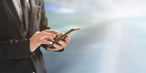 Closeup image of businessman holding and using mobile phone over blur background with copy space.