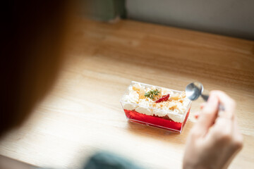 A brown-haired woman wears a green dress, preparing to eat Jelly dessert which is placed on a wooden table in a coffee shop.