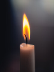Close-up of a shining and glowing candle light with a warm flame and a blurry dark background