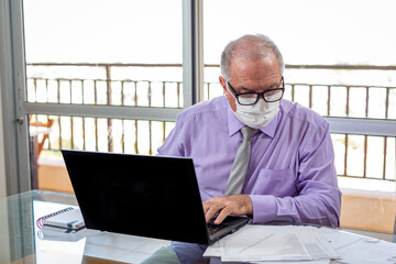Sir typing on the notebook, working on the home office system in times of pandemic by the Corona virus. Sir works at home wearing a shirt and tie and wearing a mask.