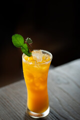 orange juice decorated with kaffir lime leave on table near dark wall