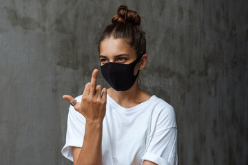 Young beautiful woman in a black mask shows the middle finger. Girl in protective mask