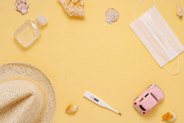 Fototapeta na wymiar Summer car trip flat lay composition top view with copy space; Image of Protective medical mask, disinfectant, thermometer, straw hat, toy car, shells on a yellow background.