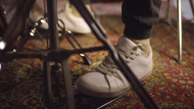 Unrecognizable man using bass drum pedals while playing drums in garage, close-up shot footage of his feet