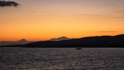 Naklejka premium Bright orange-yellow sunset in the resort city of Gelendzhik. A colorful summer landscape, a view of the sea Bay, mountains and a passing pleasure yacht. Black sea coast