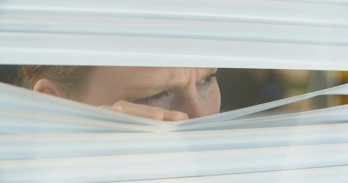 Curious woman looking out through Venetian window blinds, close up shot.