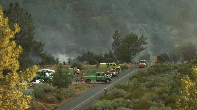 Distant shot of multiple firefighting vehicles at operating head quarters to fight Kern River wildfire, closed road, smoke in background