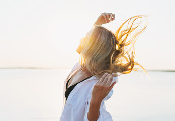 Beautiful smiling blonde young woman in white shirt on pier on sunset