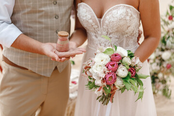 Bride and groom holding bottle with sand after tropical wedding ceremony on the beach