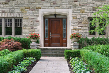 Stone faced house with shrubbery and elegant wooden front door with sidelights