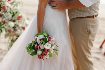 The view of the newlyweds legs standing on the beach. The view of the perfect wedding bouquet