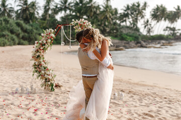 Brid and goom kiss and hugs under round wedding arch in rustic boho style, beach wedding ceremony...