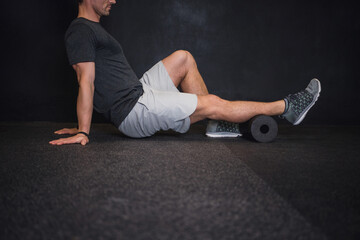 Athletic man using a foam roller to relieve sore muscles and recovers by massaging fascia after a workout.