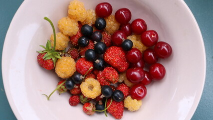 fresh berry platter from the garden harvest on a light plate top view, colored natural mosaic of smell and taste