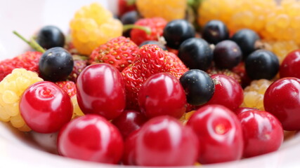 semi-blurred berry summer bright background of ripe garden berries: white raspberries, black currants, strawberries and cherries close-up