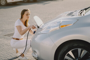 Charging electro car at the electric gas station. Woman standing by the car.