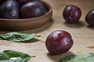 Ripe blue plum with drops on a wooden table against the background of a ceramic plate with plums....