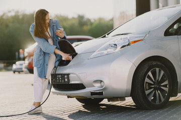 Charging electro car at the electric gas station. Woman standing by the car.