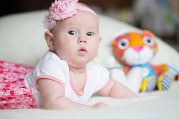 Adorable 3 months old baby girl lying on bed among her toys