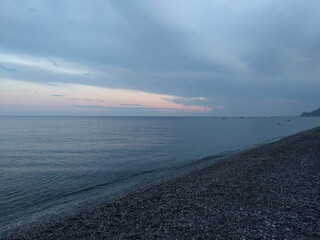 Obraz premium Coastline with pebble stones, sea, horizon line and sunset light on background, Sicily, Italy.