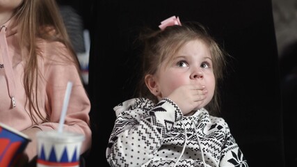 Close up of little girl is watching a movie and eating popcorn