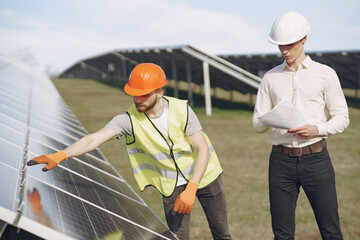 Businessman and worker near solar energy batteries. Business client showing photovoltaic detail to foreman. Two men making deal.