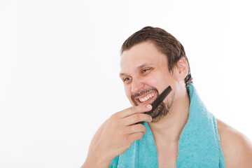 a man combs his stubble. the guy is brushing his beard. morning treatments in the bathroom. blue towel around her neck. isolated on a white background. copy space