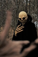 Death in the dark forest.Halloween. Man in death costume and skull mask on bare leafless autumn...