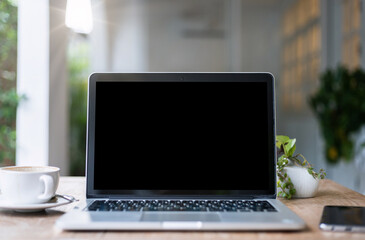 Fototapeta premium Mockup of laptop computer with empty screen with coffee cup and smartphone on table of the coffee shop background,Black screen