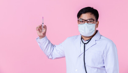 Asian man doctor therapeutic wears hygiene protective mask ,stethoscope with positive emotions advising holding a syringe to the side eyes looking at camera in isolated on pink blank copy space