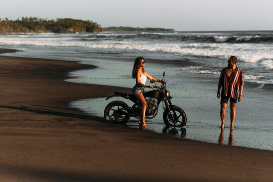 Couple on a motorbike on the beach. A couple in love on the beach meets the sunset. Beautiful couple on a bike. Travel on a motorbike. Lovers on the beach. Journey to the island of Bali. Copy space
