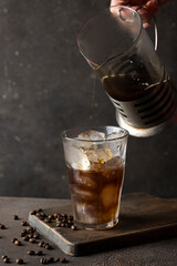 Cold coffee pouring into the glass with ice. Making Ice coffee concept.