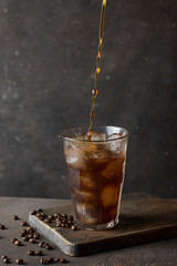 Cold coffee pouring into the glass with ice On brow baclground with ice and coffee beans.