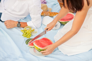 Obraz na płótnie Canvas Woman cut red ripe watermelon into pieces. Family beach picnic.