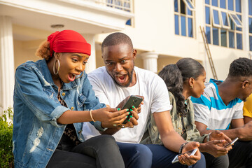 excited young africans feeling excited while looking at a mobile phone, sitting with friends