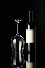 Bottle of red wine and an inverted wine glass on a black background.